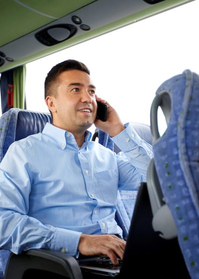 transport, tourism, business trip and people concept - smiling man with smartphone and laptop calling in travel bus